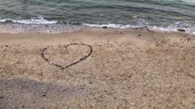 Bir deniz dalgası yalnız bir plajda taşlarından yapılmış bir kalp yıkar. Sevgililer günü kavramı, 4k video
