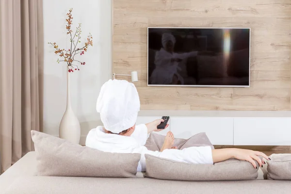 Frau sitzt auf einer Couch mit Handtuch auf dem Kopf vor dem Fernseher — Stockfoto