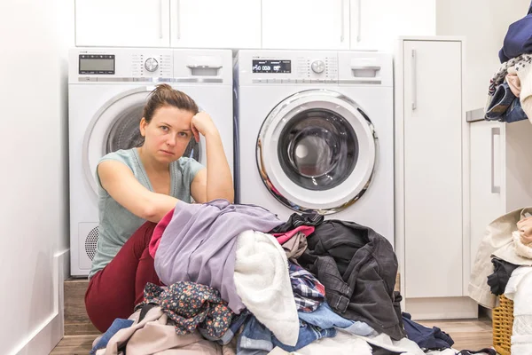 Upset woman in laudry room sitting ona floor with dirty clothes — Stock Photo, Image