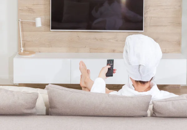 Tv izlerken başında havlu ile bir kanepede oturan kadın — Stok fotoğraf
