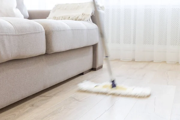 Piso de limpieza con fregona blanca cerca del sofá —  Fotos de Stock