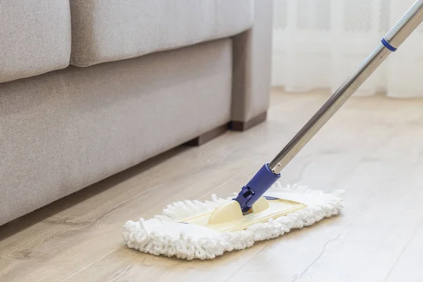 Cleaning floor with white mop near sofa — Stock Photo, Image