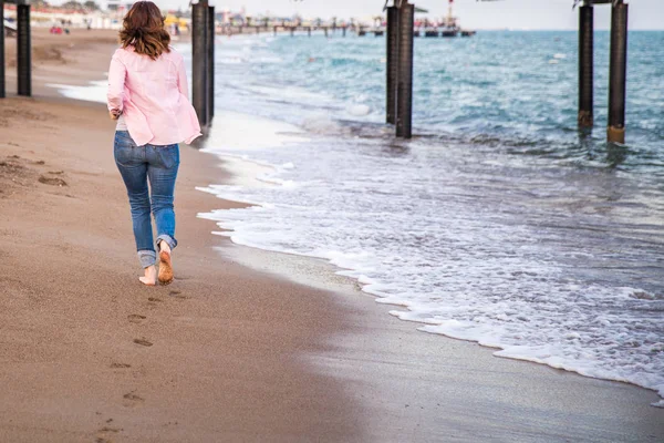 Frau in Jeans läuft bei Sonnenuntergang am Strand Sand — Stockfoto