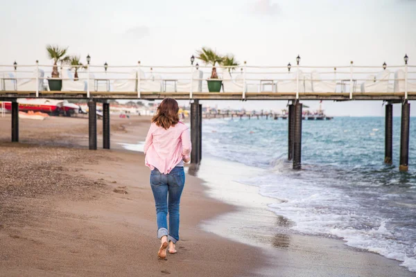 Mujer con jeans corriendo al atardecer en la arena de la playa —  Fotos de Stock