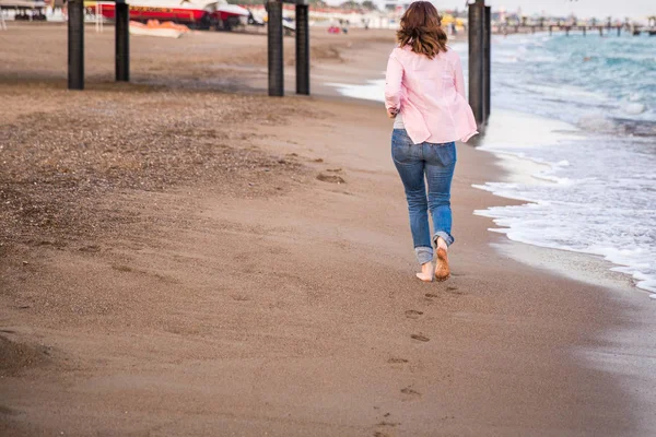 Frau in Jeans läuft bei Sonnenuntergang am Strand Sand — Stockfoto