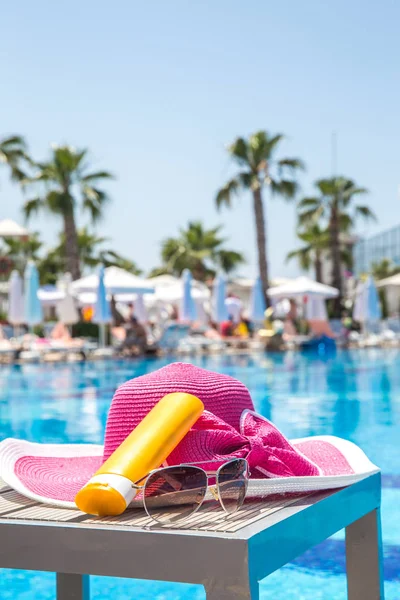 Bouteille de crème solaire, chapeau et lunettes de soleil à côté de la piscine de l'hôtel — Photo