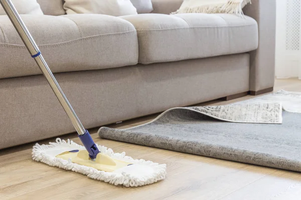 Piso de limpeza com esfregona sob tapete na sala de estar — Fotografia de Stock