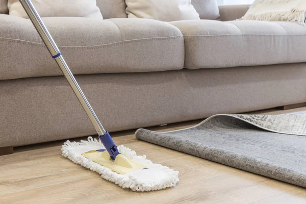 Piso de limpieza con fregona debajo de la alfombra en la sala de estar —  Fotos de Stock