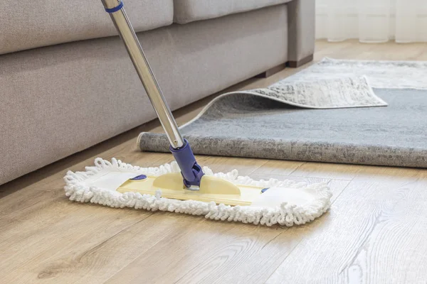 Piso de limpieza con fregona debajo de la alfombra en la sala de estar —  Fotos de Stock