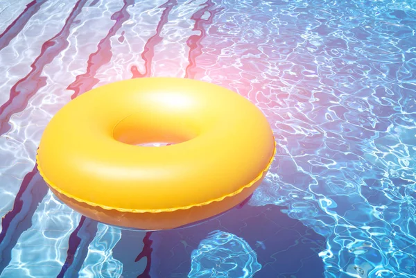 Inflatable yellow inner tube floating in clear blue waters in pool with bright light — Stock Photo, Image