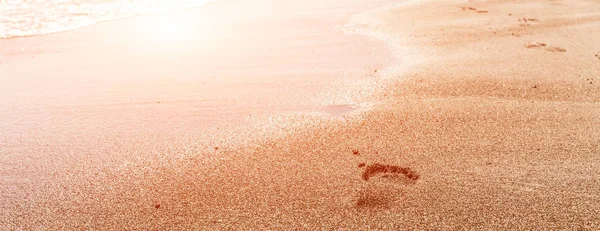 Güneş parlaması ile gün batımı nda plaj, dalga ve kadın ayak izleri — Stok fotoğraf