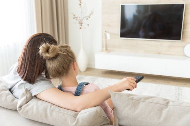 Anne ve kızı kanepede oturarak televizyon izlerken
