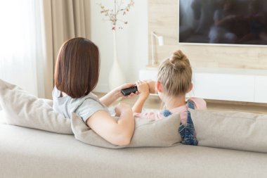 Anne ve kızı kanepede oturarak televizyon izliyor, uzaktan kumanda için savaşıyor