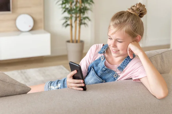 Kleines Mädchen spielt zu Hause auf der Couch mit dem Handy — Stockfoto