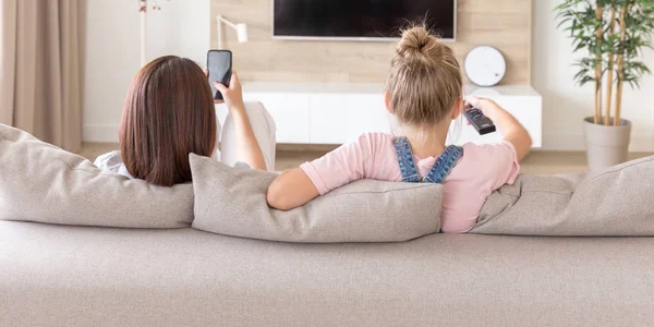 Mother and daughter sitting on couch watching tv in living room — Stock Photo, Image