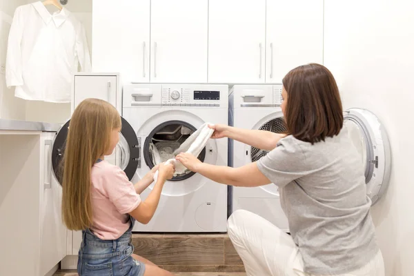 Мати і дочка помічник в пральні біля пральної машинки і сушарки знімають чистий одяг — стокове фото