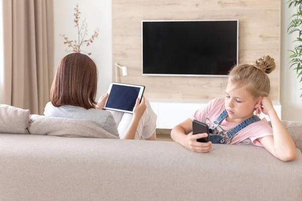 Mädchen sitzt auf der Couch und schaut etwas Interessantes im Handy, während Mutter fernsieht — Stockfoto