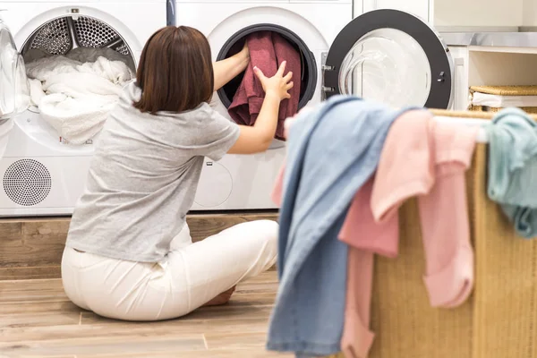 Mujer joven cargando lavadora y una cesta llena de ropa sucia en la sala de lavandería — Foto de Stock