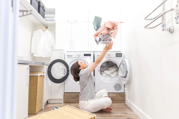 Щаслива родина домогосподарка в пральні з пральною машинкою кидає одяг вгору — стокове фото