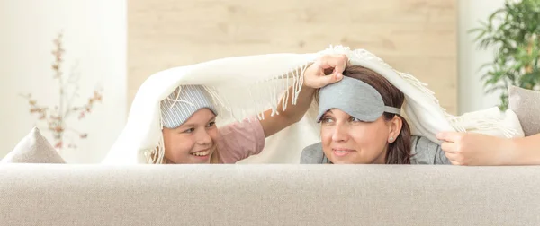 Mother and daughter wearing sleeping mask having fun on couch with copy space — Stock Photo, Image