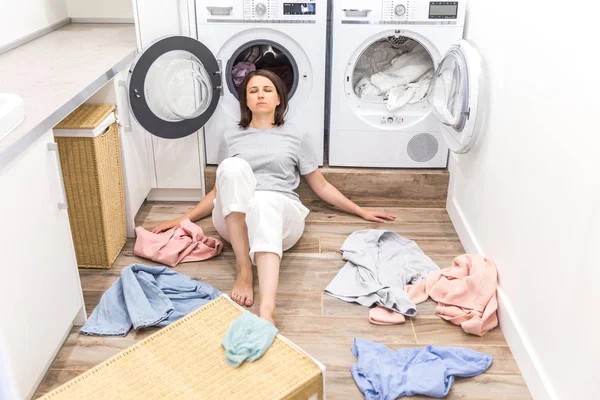 Mujer triste sentada en laudry habitación con una pila de ropa sucia — Foto de Stock