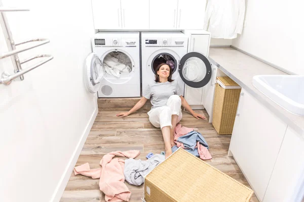 Щаслива жінка домогосподарка в пральні біля пральної машинки з брудним одягом — стокове фото