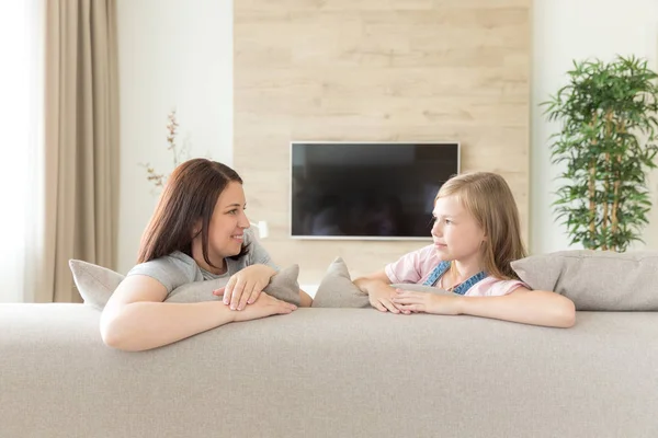 Pessoas e conceito de família - menina sorridente feliz com a mãe abraçando no sofá em casa — Fotografia de Stock