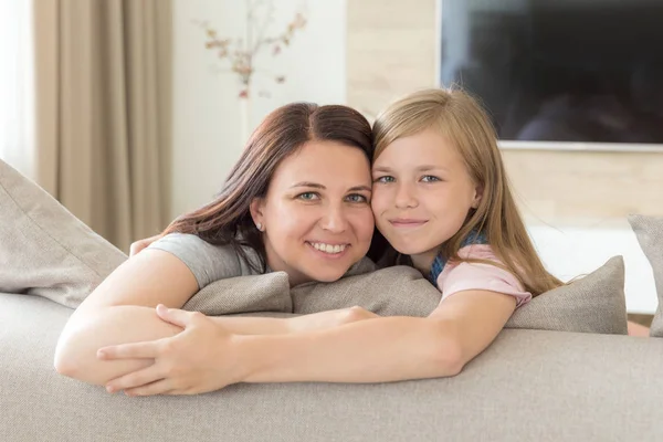 Lidé a rodiny koncept - šťastná usměvavá dívka s matkou objímání na gauči doma — Stock fotografie