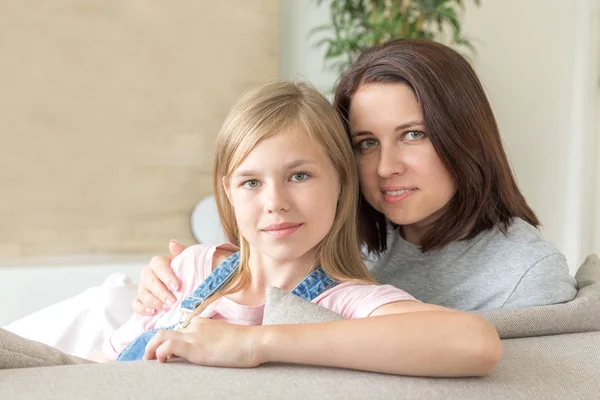 Pessoas e conceito de família - menina sorridente feliz com a mãe abraçando no sofá em casa — Fotografia de Stock