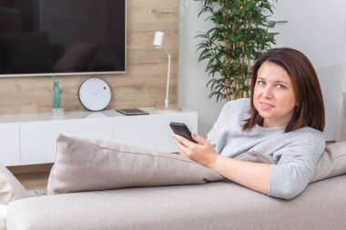 Seyir onun akıllı telefon ve kanepede otururken gülümseyen genç kadın