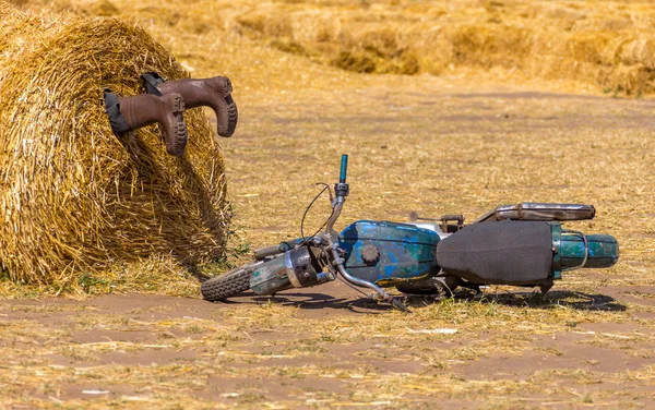 Een motorycle in de buurt van de hooiberg en laarzen in de stapel stro. crash humor concept decoratie — Stockfoto