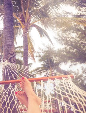 Palmiye ağaçları ve parlak gün batımı ile bir hamakta Woman Feet. Turuncu renk tonu ile tatil konsepti