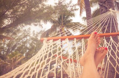 Palmiye ağaçları ve parlak gün batımı ile bir hamakta Woman Feet. Turuncu renk tonu ile tatil konsepti