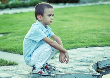 Üzgün bir çocuk sokakta tek başına oturuyor. Mutsuz yalnız çocuk. Mavi ton