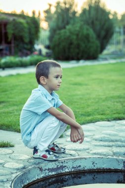 Üzgün bir çocuk sokakta tek başına oturuyor. Mutsuz yalnız çocuk. Mavi ton