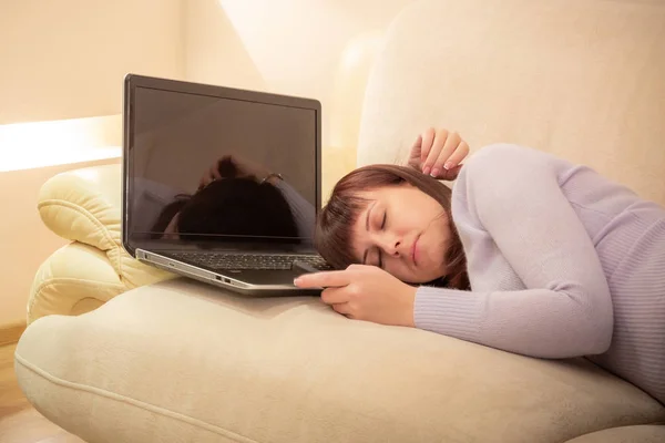 Tired freelance worker woman sleeping right on her laptops keyboard on a couch — Stock Photo, Image