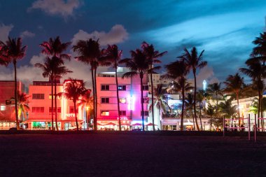 Gün batımında Miami Beach Ocean Drive otel ve restoranları. Geceleri palmiye ağaçları ile şehir silueti. Güney sahilinde Art deco gece hayatı