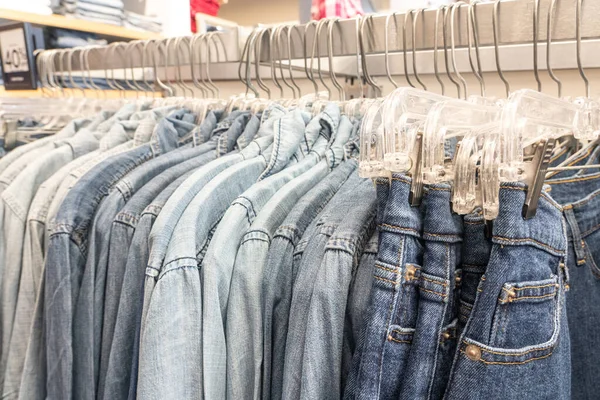 Hombres vaqueros vaqueros camisas ordenadas en perchas de ropa en un armario de tienda armario carril — Foto de Stock