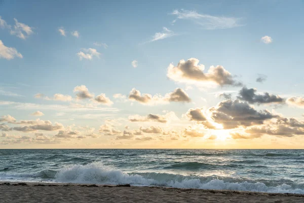 Sol naciente en el horizonte sobre un océano o mar. En el cielo azul nubes blancas — Foto de Stock