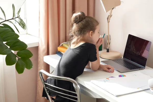 Kíváncsi kislány laptopot használ az asztalnál. — Stock Fotó