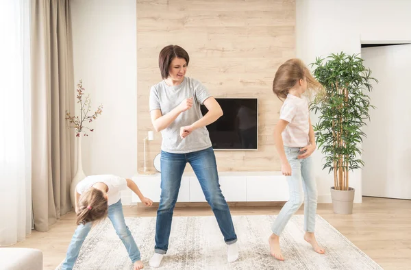 Glückliche Mutter und zwei Töchter haben Spaß beim Tanzen im Wohnzimmer. Mutter lacht und genießt lustige Lifestyleaktivitäten mit Teenager-Mädchen zu Hause zusammen. — Stockfoto