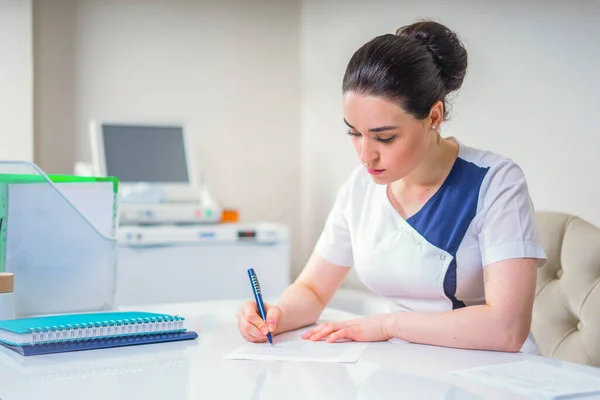 Ofisinde oturan genç bayan doktor bir şeyler yazıyor. Sağlık ve Tıp Konsepti — Stok fotoğraf