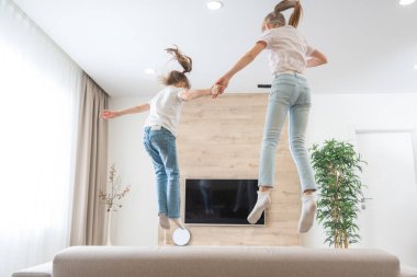 İki kız kardeş oturma odasında kanepede zıplayıp eğleniyorlar.