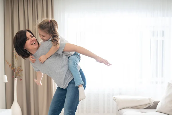 Mãe dando passeio de piggyback alegre para sua filha, se divertindo em casa, mãe solteira conceito de família feliz — Fotografia de Stock