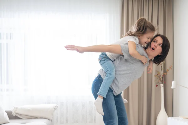 Mãe dando passeio de piggyback alegre para sua filha, se divertindo em casa, mãe solteira conceito de família feliz — Fotografia de Stock