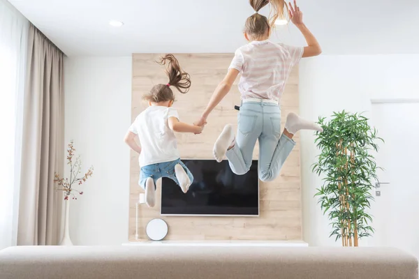 Dos hermanas saltando en el sofá en sala de estar divirtiéndose — Foto de Stock