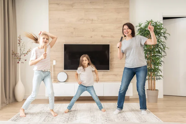 Glückliche Mutter und zwei Töchter, die Spaß daran haben, Karaoke-Lieder in Haarbürsten zu singen. Mutter lacht und genießt lustige Lifestyleaktivitäten mit Teenager-Mädchen zu Hause zusammen. — Stockfoto