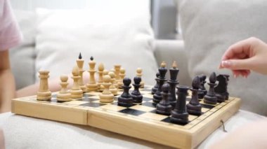 Anne ve kızı satranç oynuyor ve oturma odasında bir kanepede oturuyor.