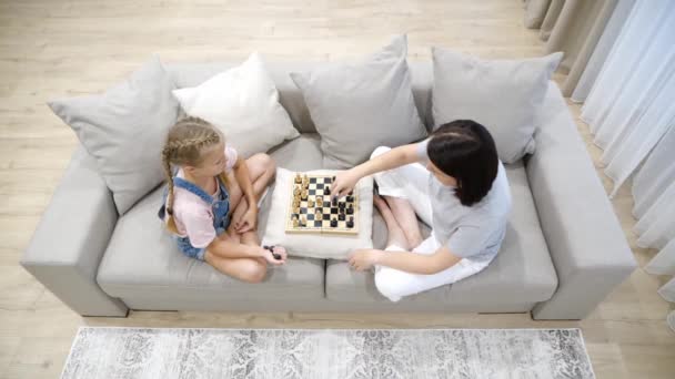 Mor och dotter spelar schack och sitter i soffa i vardagsrummet — Stockvideo