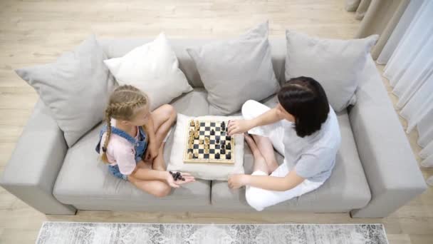 Mor och dotter spelar schack och sitter i soffa i vardagsrummet — Stockvideo